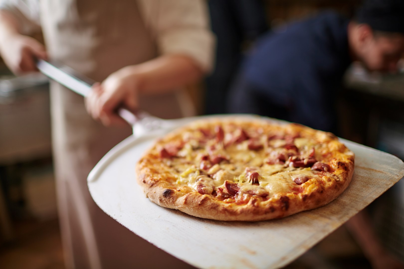 cook with a cooked pizza on a pizza paddle